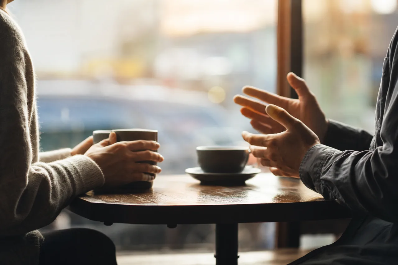 Two people talking across a cafe table with coffee cups